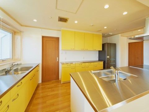 キッチンは広々としており、木製のドアとガラス窓が１ヶ所ある。流し台が２ヶ所と冷蔵庫１台が設置され、シンクや戸棚の扉は黄色に統一されている。