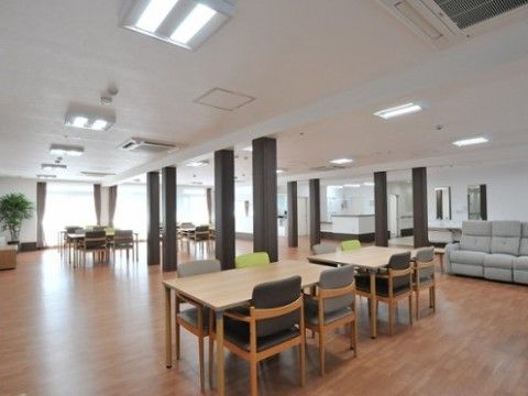 木目調のダイニングテーブルが十分な間隔を空けて設置されている、天井が高くて広い食堂