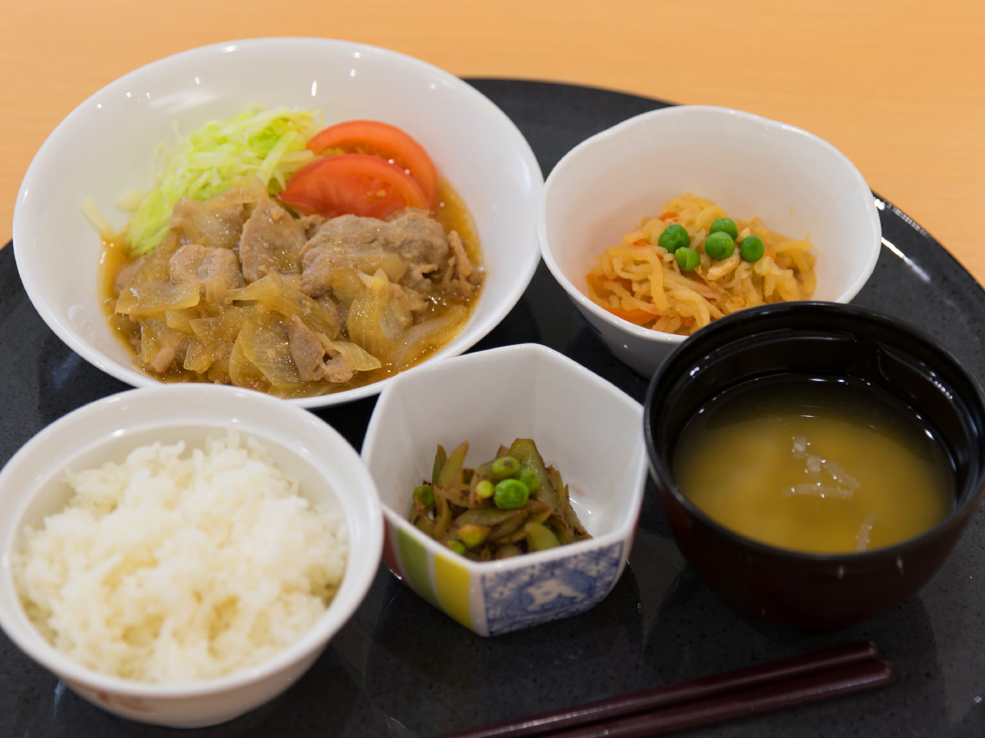 ダークグレーの扇型のお盆に陶器の器で盛られた料理が5品目ある。野菜が中心で赤、黄、緑を利用して彩りよく盛り付けられている。