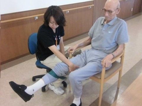 椅子に座って足のリハビリをする入居者様を、スタッフがサポートしている様子