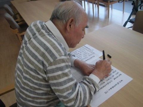 入居者様がテーブルで見本を横に置き、文字を書き写している様子