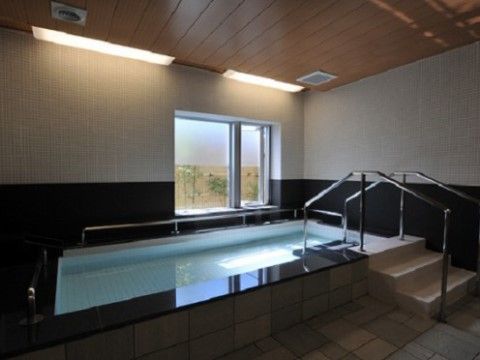 浴槽に入りやすいように階段が取り付けられ、手すりが設置されている。窓の外には木の壁と樹木が見え、和の雰囲気がある。