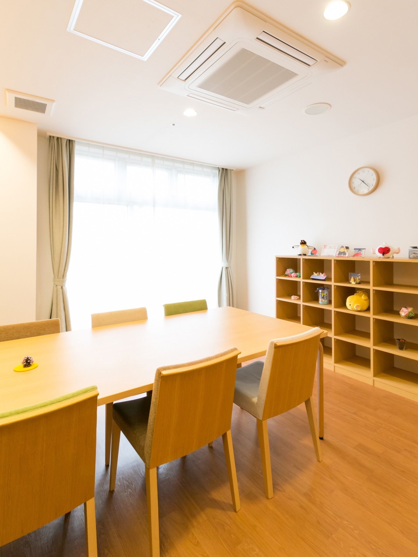 ナチュラルな色合いの木目で統一された部屋である。奥にはオープン棚があり、飾りものが置かれている。手前にテーブルと椅子がある。