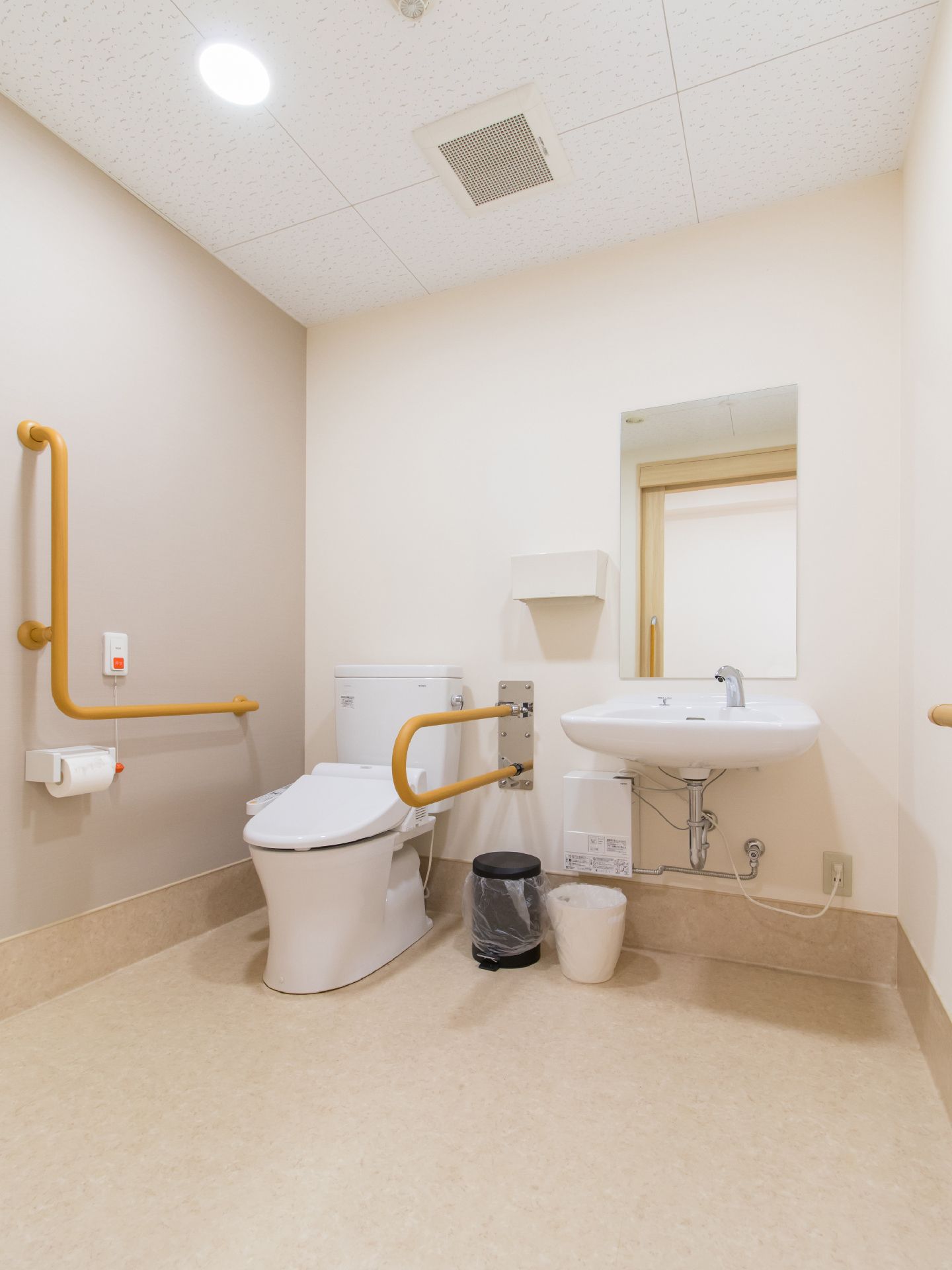 広いスペースに洋式トイレが設置されている。温水洗浄便座や可動式の手すりがあり、使いやすい。白い壁と天井で清潔感がある。