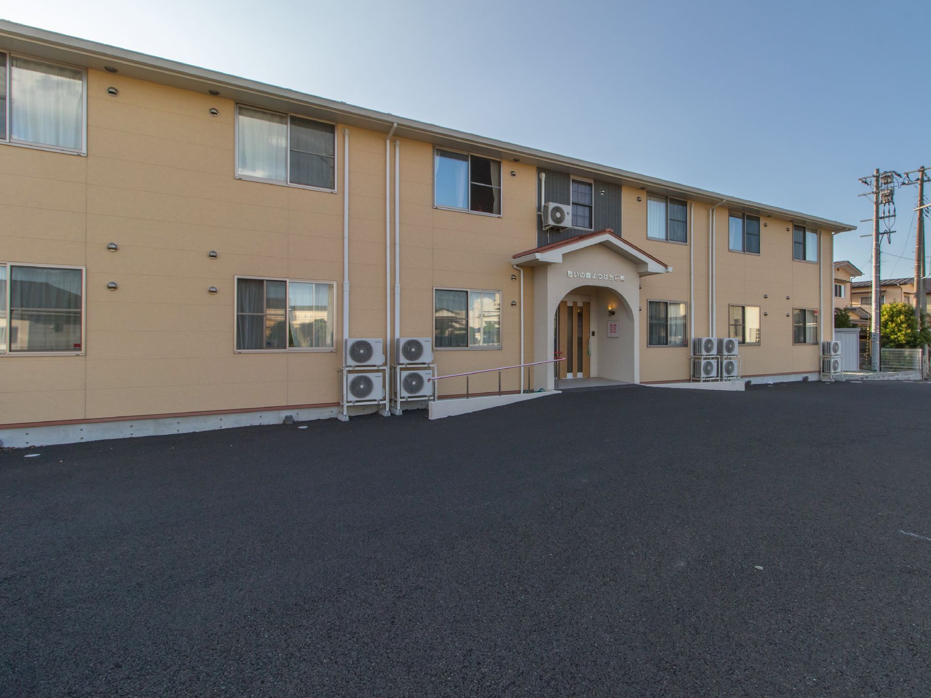 施設はベージュ系の壁で2階建てである。入口近くには手すりも完備されている。施設前には広いスペースがある。