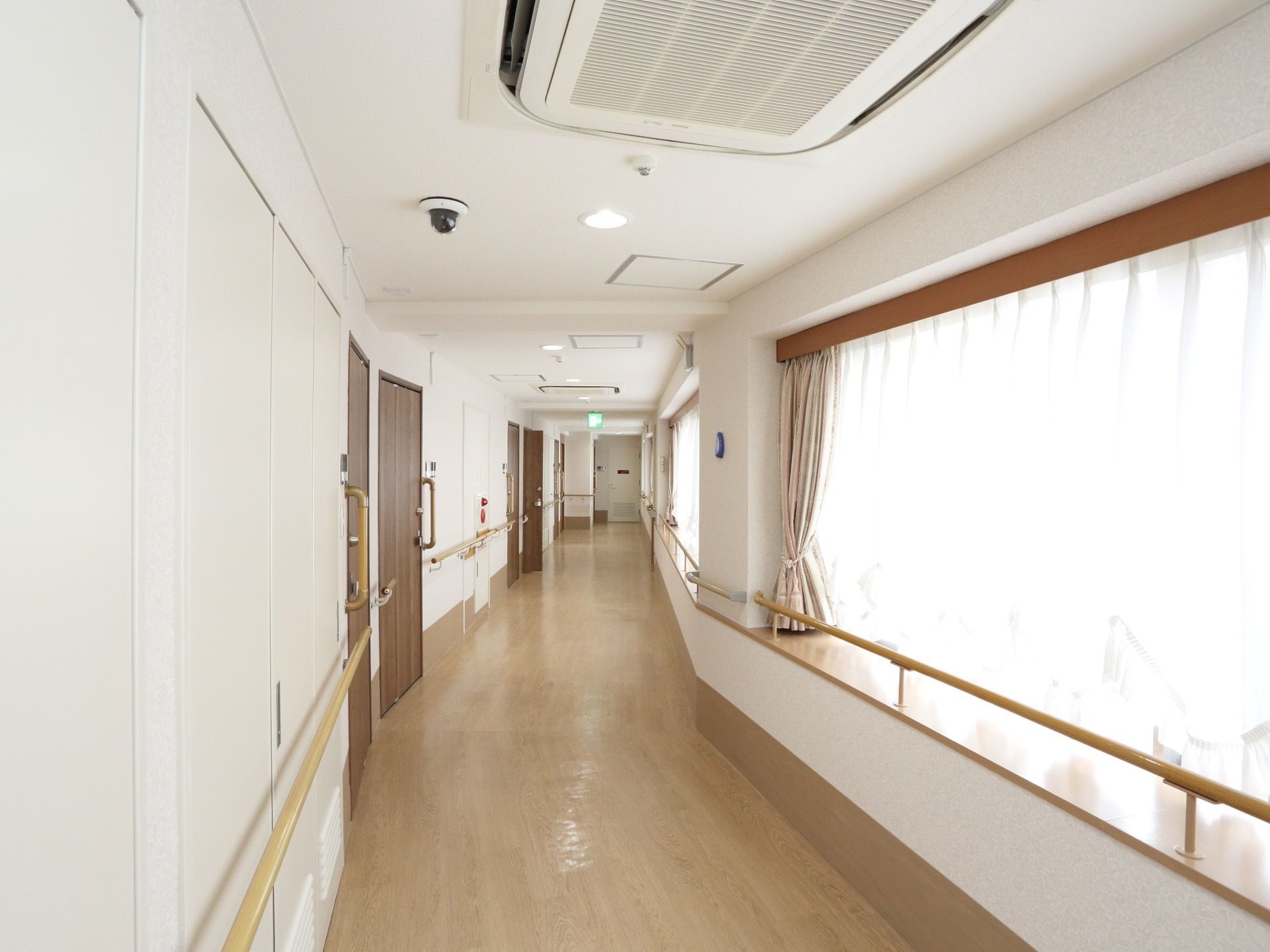 廊下の左側には居室、右側には大きな窓が並び、明るく開放感がある。安全に配慮し、両側に手すりが配置されている。