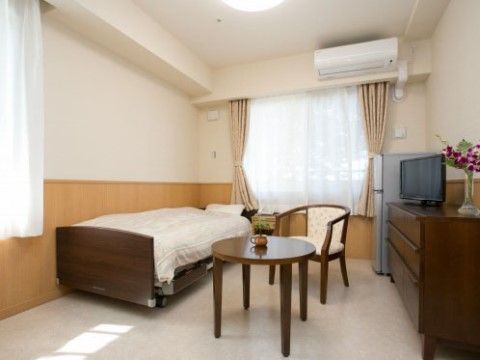 居室にベッドが置かれている。椅子やテーブル、テレビのほかに冷蔵庫も設置されている。テレビボードは収納がついている。