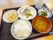 四角い黒いお盆の上に数種類のお皿をのせて一人ずつ配膳されている。ご飯にお味噌汁、焼き魚などのおかずがきれいに配置されている。