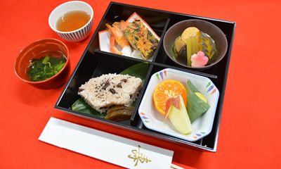 海老や野菜の煮物、リンゴやみかんのデザートに赤飯と汁物が付いたメニュー
