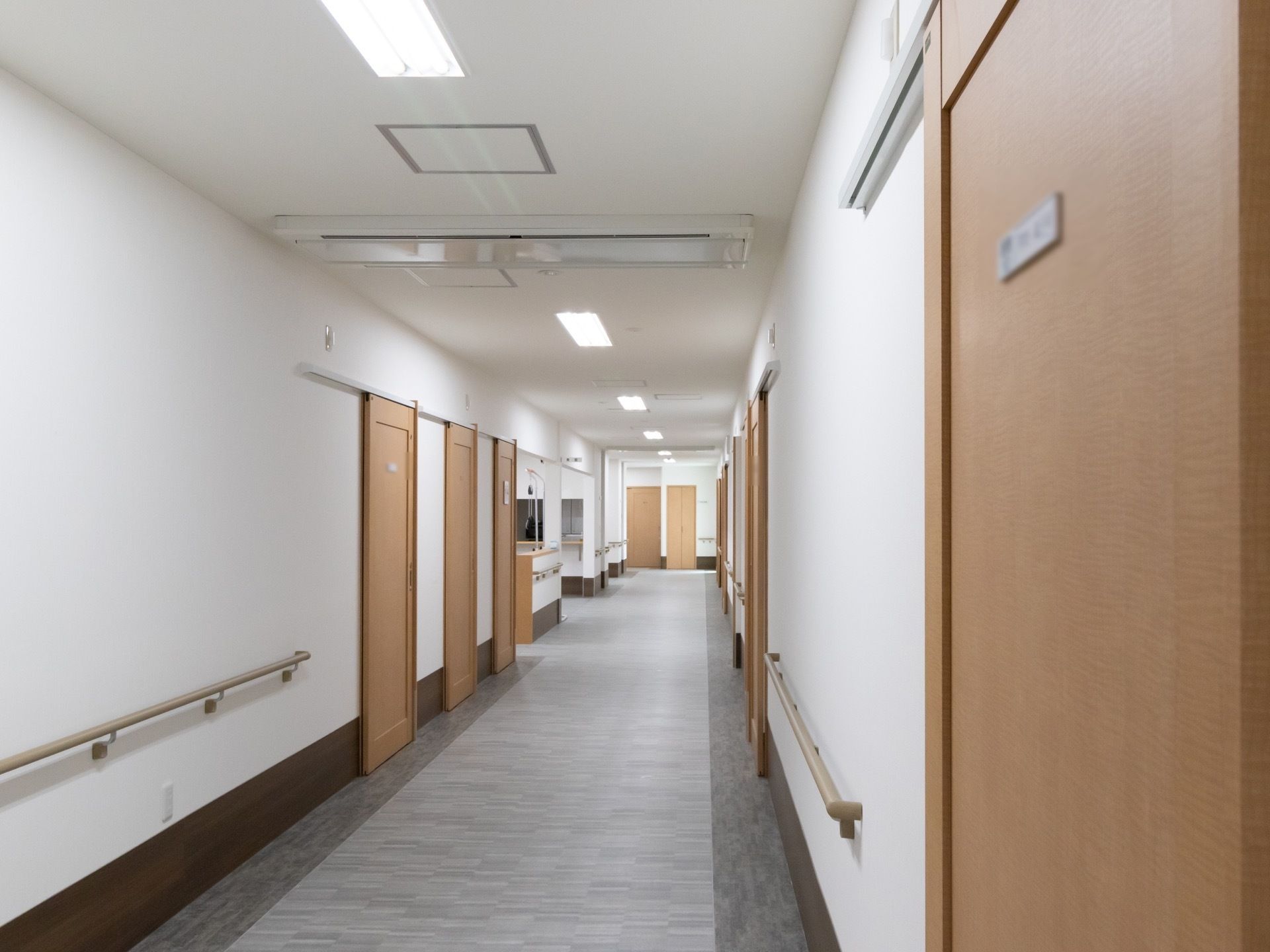 施設内の廊下の様子である。床はグレー、各ドアは同じ材質の木製風のもので統一されている。照明には直管タイプの蛍光灯が使用されている。