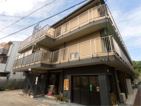 住宅街の中にある３階建てのグループホームである。２階以上には白いフェンスが取り付けられたベランダが設けられている。