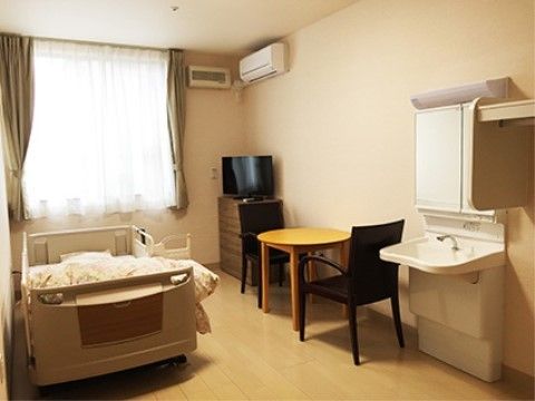 １人用テーブルが置かれており、洗面台や介護ベッド、エアコンが備わっている居室