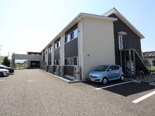 ベージュとブラウンの２階建ての建物の玄関には大きな車寄せがあり、広い駐車場もある。