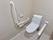 白い床と壁の個室トイレ。温水洗浄機能付きのトイレの両脇に安全のために手すりがついている。壁には緊急コールが設置されている。