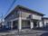 濃いグレーと薄いグレーの2階建ての建物。外壁には施設名が入っている。建物の周りは駐車場になっている。左側は公道が通っている。