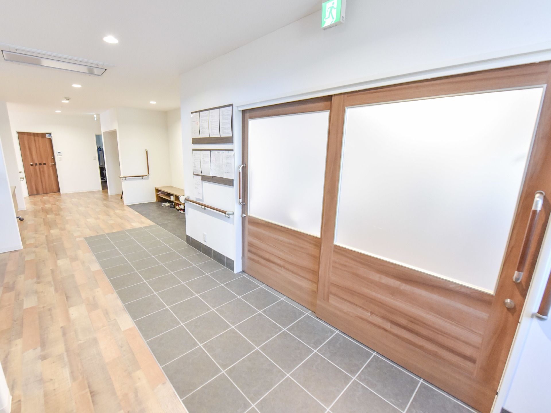 広々とした廊下には、木目調の大きな引戸が取りつけられている。壁には掲示物が張られ、横長の椅子も設置されている。