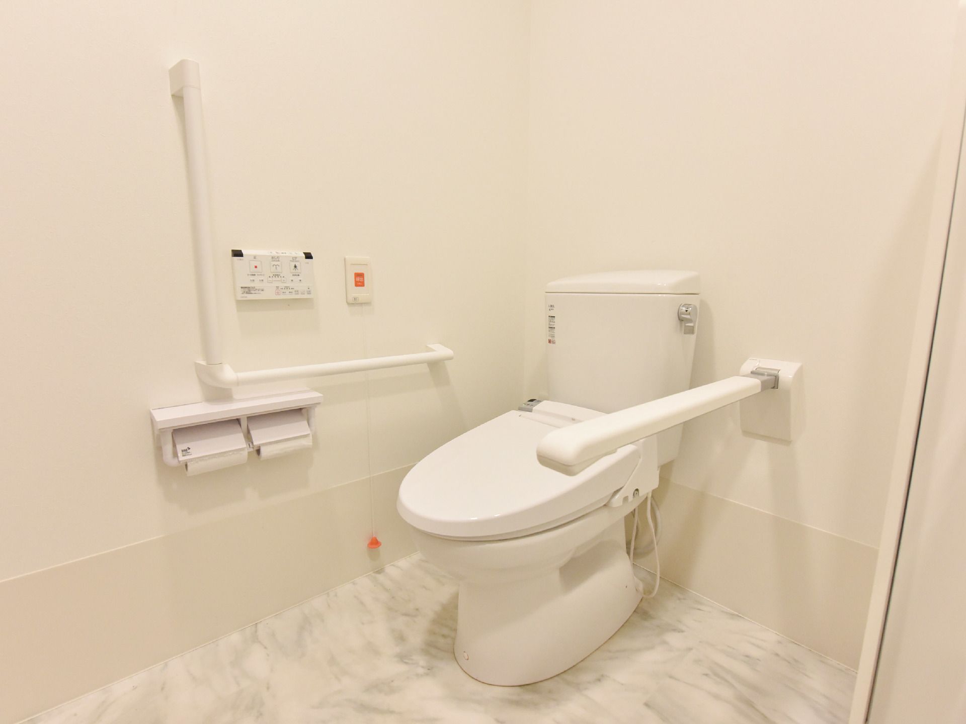 タンク付きのトイレの設置された室内は、白を基調とした内装となっている。トイレの両側には手すりが設置されている。
