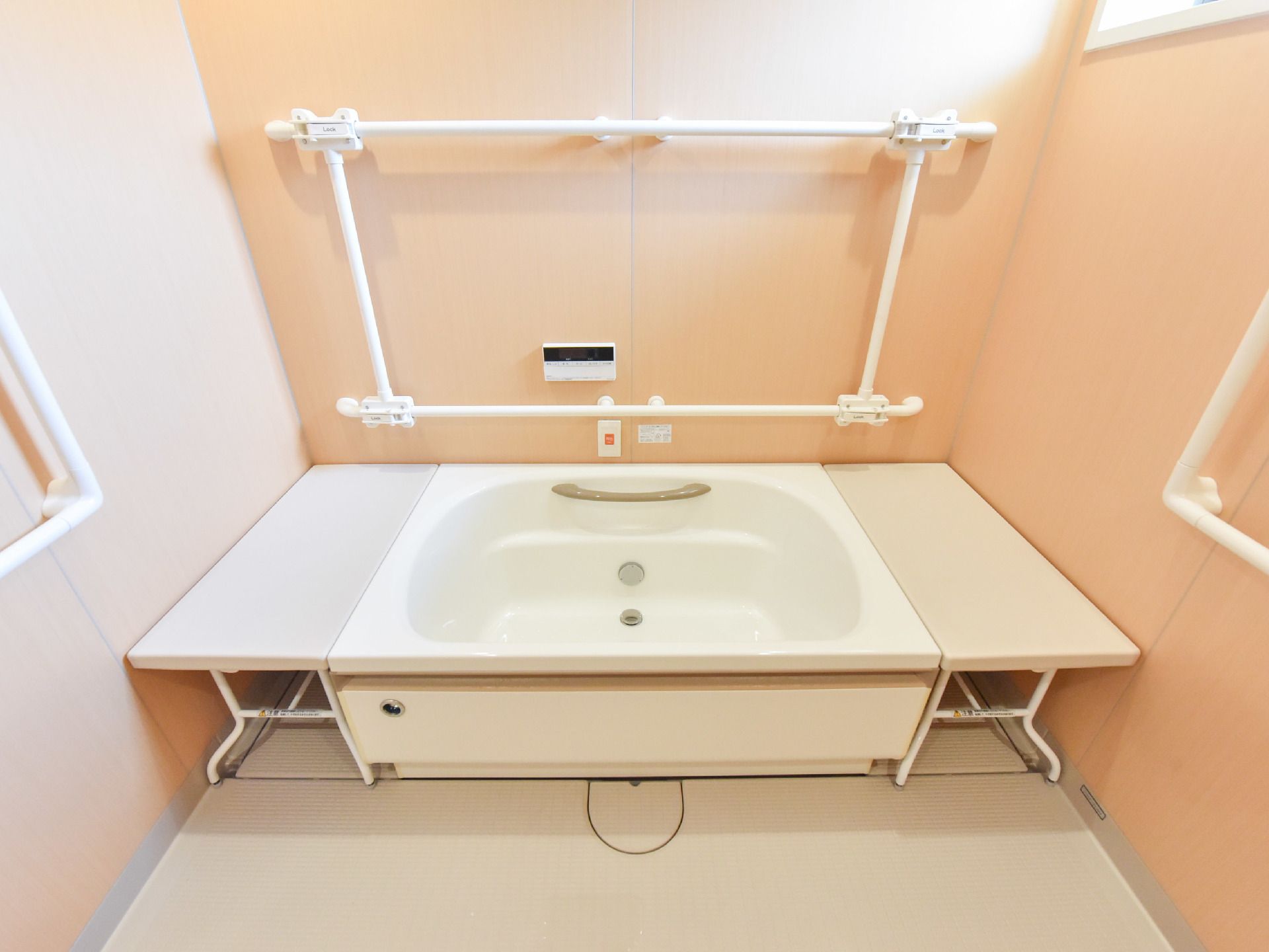 ベージュ色の壁に、四角く手すりが取りつけられてる。浴槽の両側には、取り外し可能な補助台も設置されている。