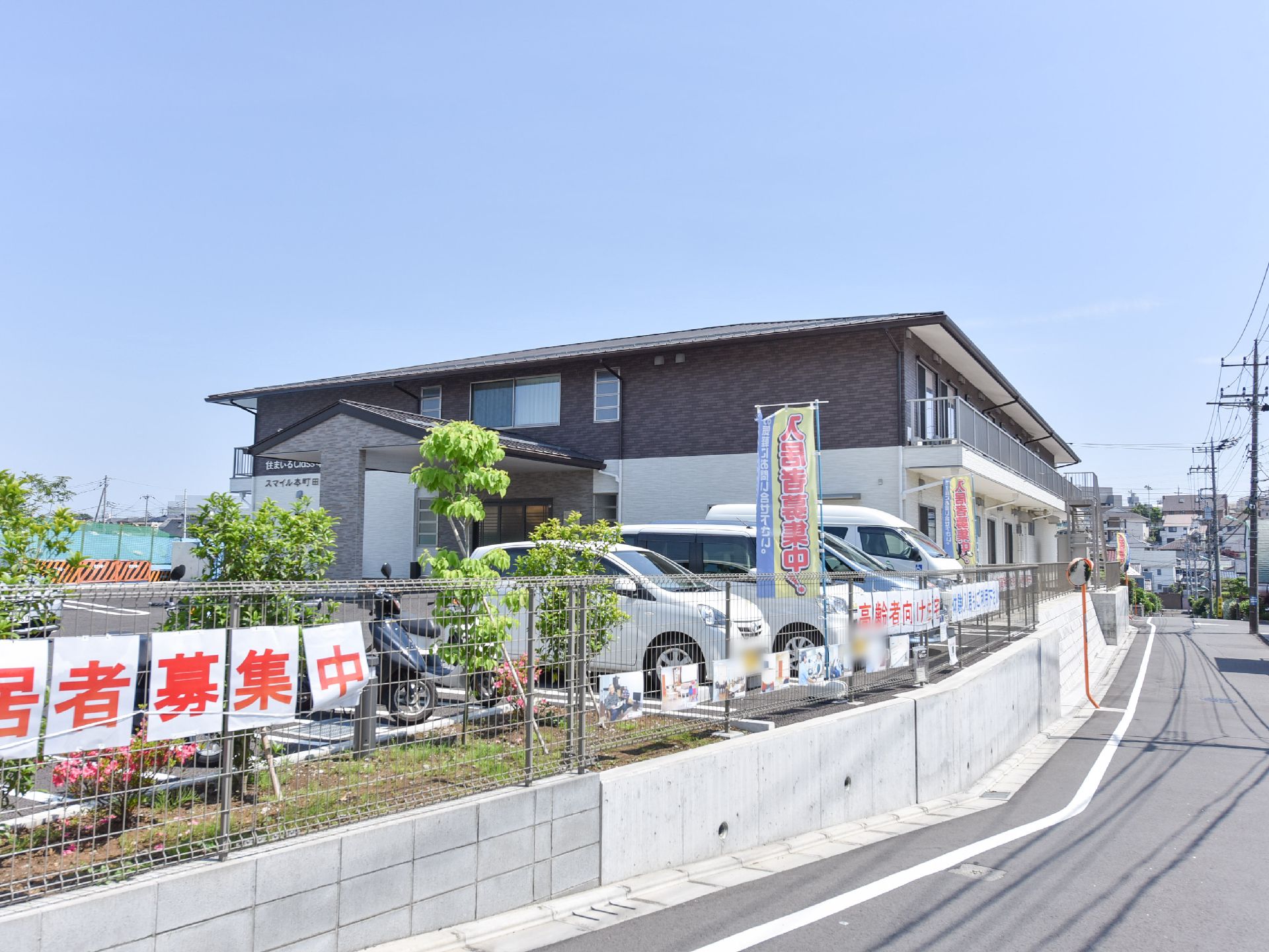 施設の隣りには、広々とした駐車場スペースが確保されている。駐車場には、自動車やスクーターが停められている。