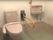 横側に小さめのシンプルな洗面台を備えたトイレスペースである。便座の傍に可動式の手すりを設置し、必要ない時は上にあげておくことができる。