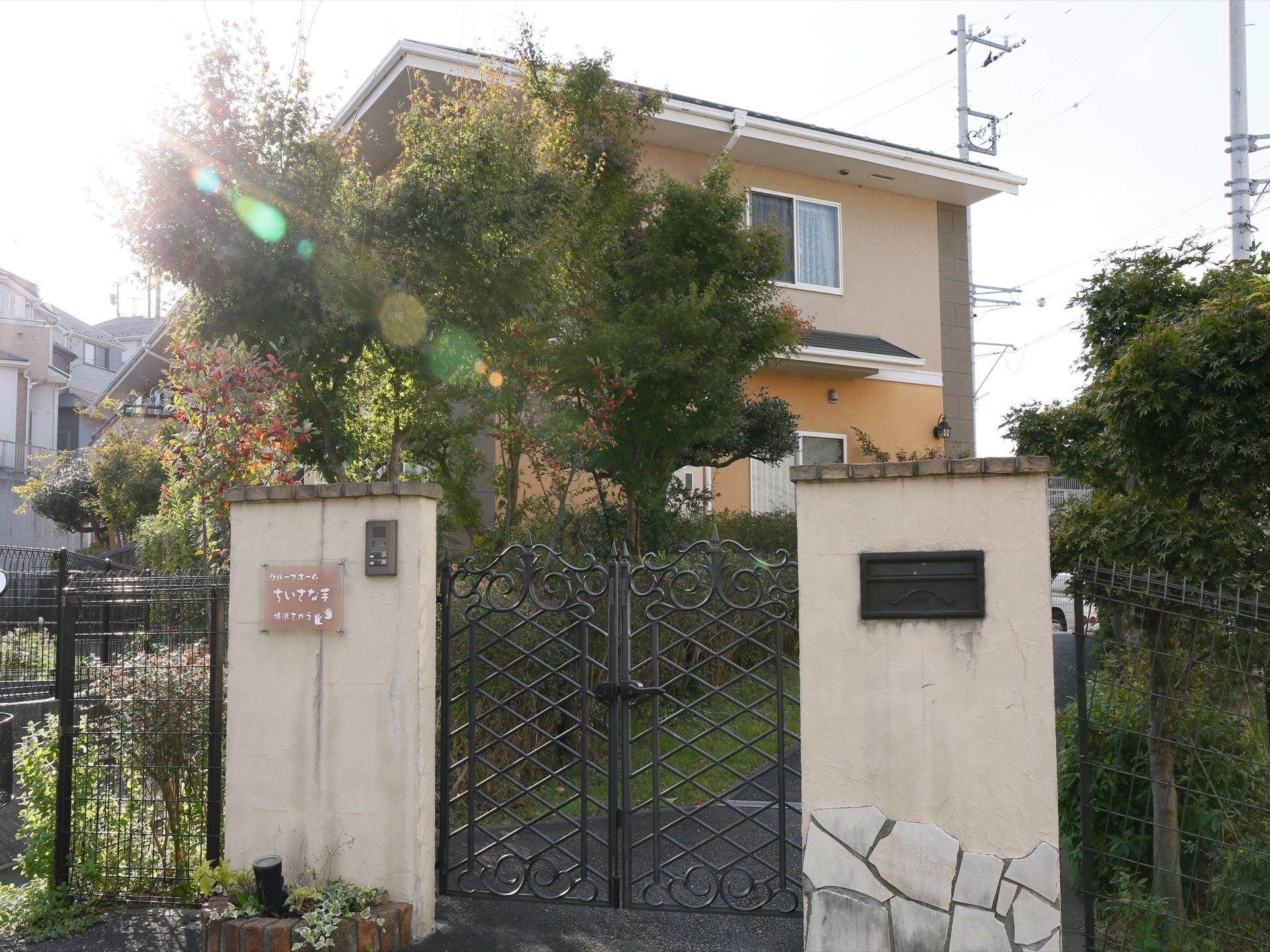 施設は静かな住宅街にある。敷地には沢山木々が植えられ、緑が豊富な環境。敷地の入口には門が取り付けられ、横にはインターフォンが付いている。