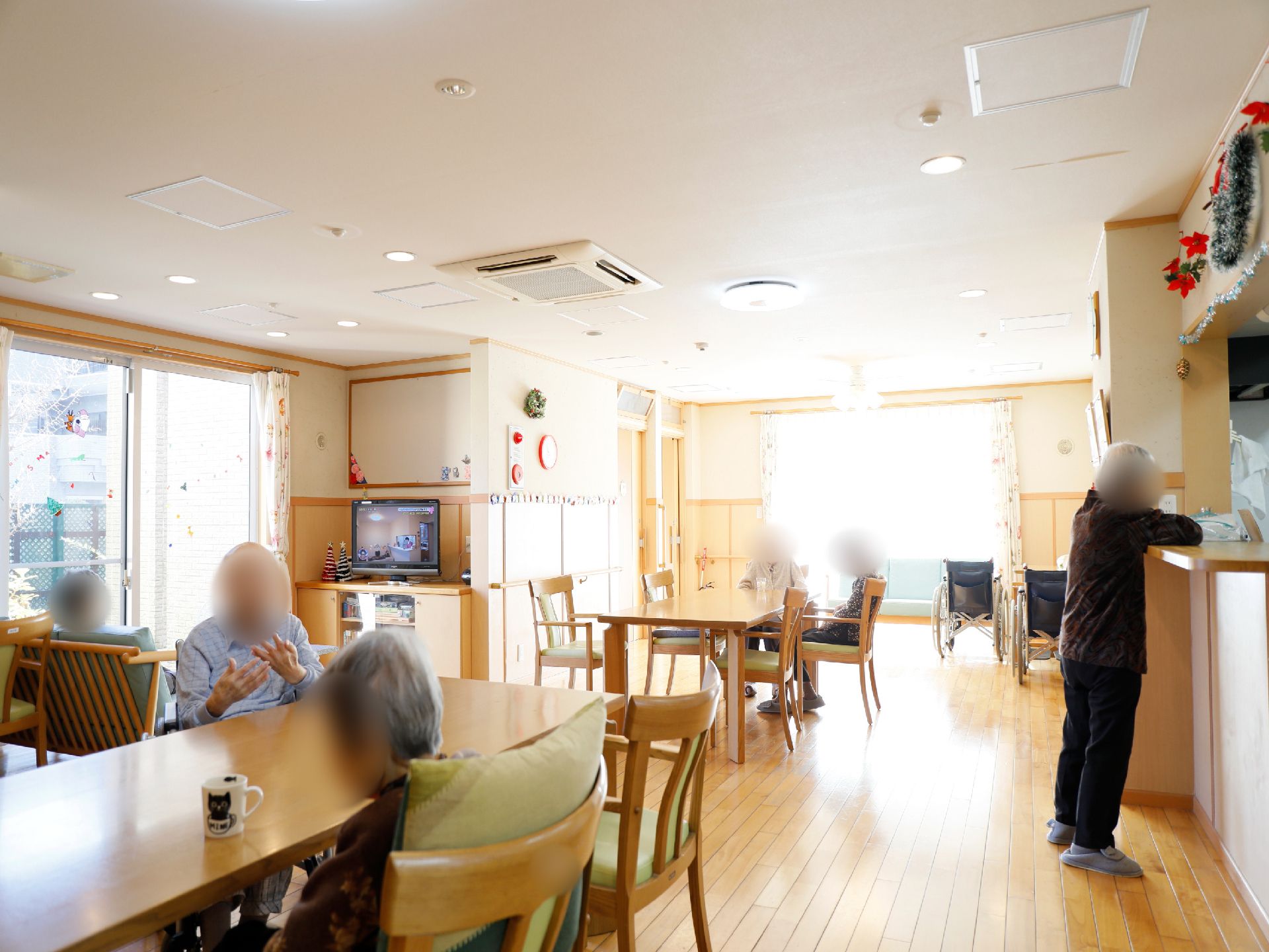 リビングに入居者様たちが集まっている。テレビ鑑賞をしたり、歓談をしたりしている。室内は、クリスマスの飾りつけがされている。