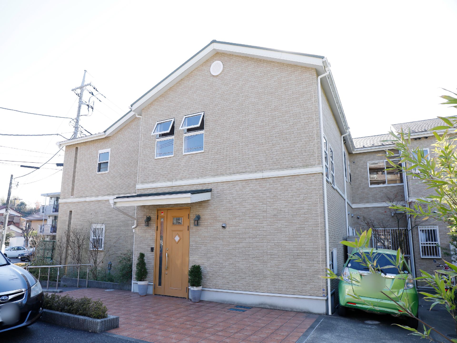 建物は、2階建ての一軒家風の造りである。周囲は段差がなく舗装されており、車が2台停車している。玄関周りに植物が飾られている。