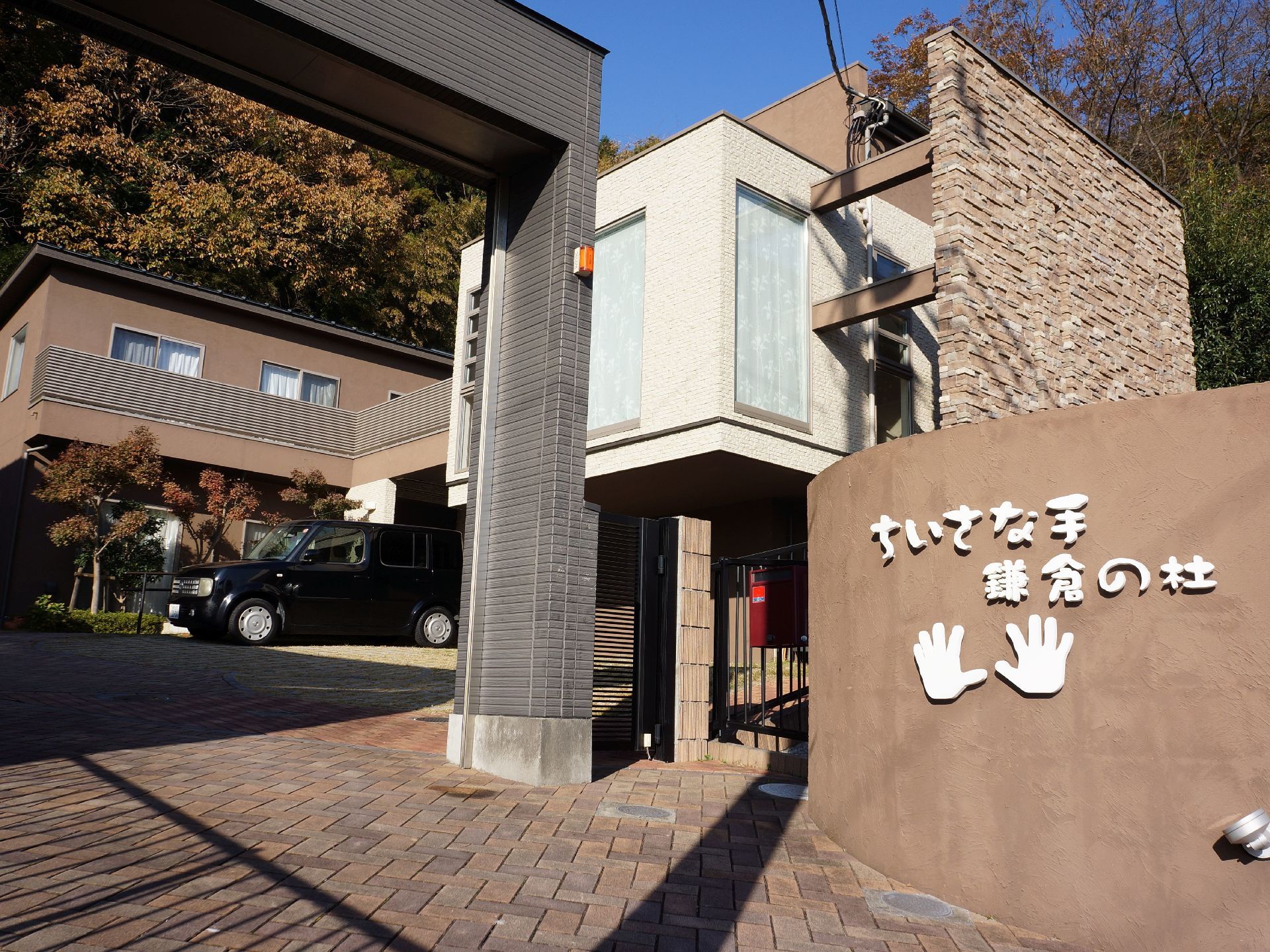 施設の敷地入口に茶色い壁があり、施設名が大きく表示されている。黒いゲートがあり、シャッターがついている。