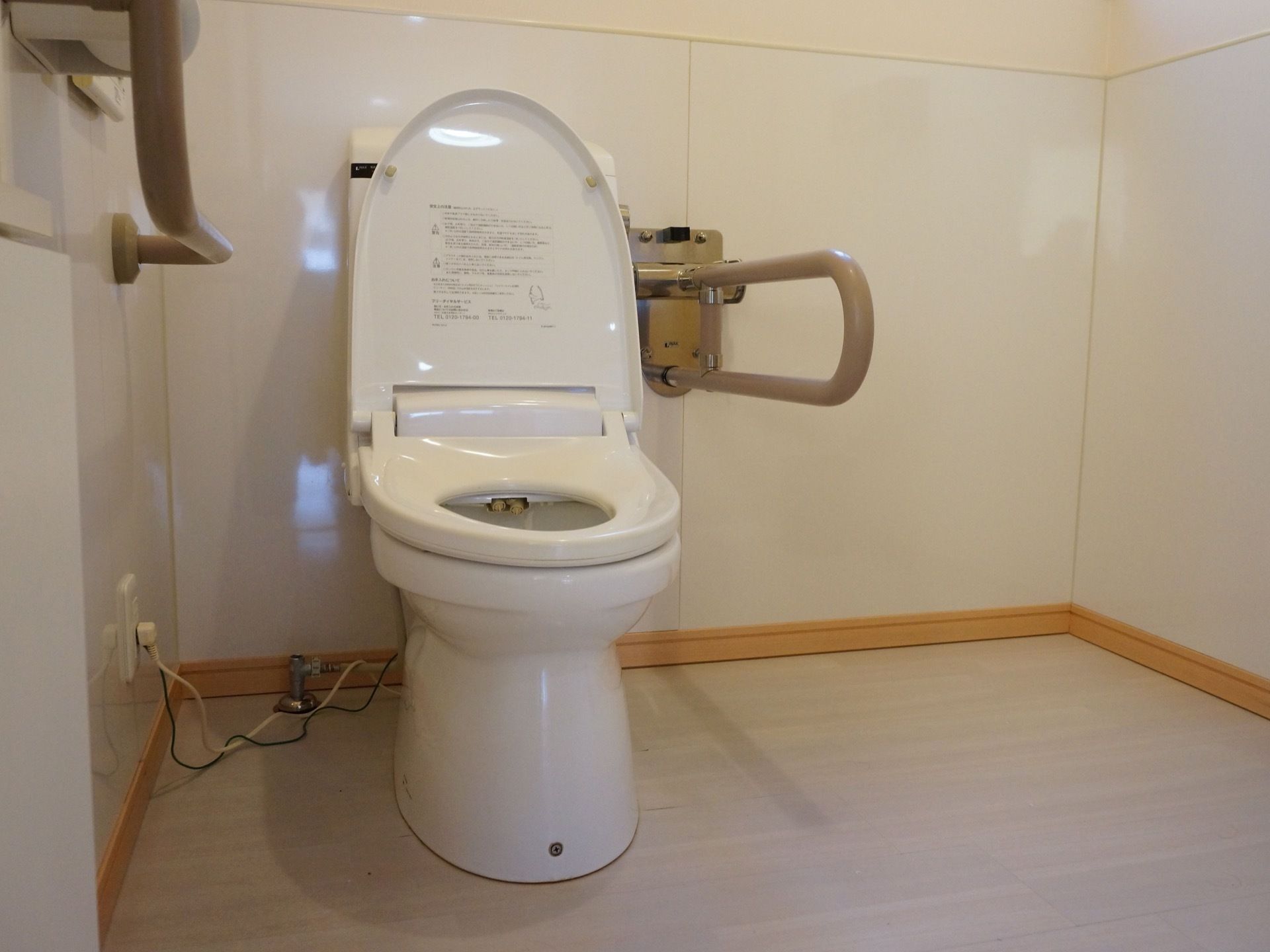 施設内にある、洋式トイレ。右壁に操作スイッチと手すりが付いている。また、左手には可動式の手すりがある。