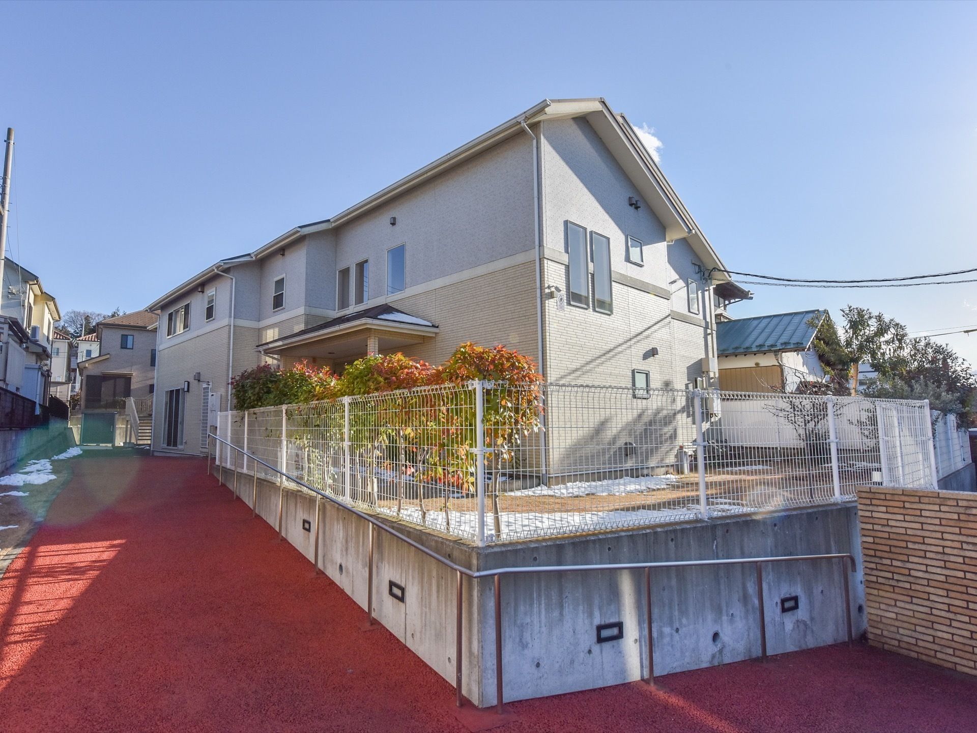 施設へと続く通路。建物は少し高い場所にあり、敷地がフェンスで囲まれている。通路沿いに手すりが設置されている。
