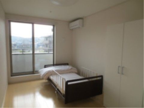 壁に沿って介護ベッドが置いてあり、窓側に掛け布団が畳んで置いてある。ベッドには、柵が２つ付いている。