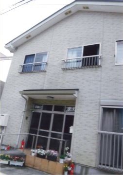 グレーの外壁で、一軒家のような外観の2階建ての建物である。入口には植物が飾られており、アットホームな雰囲気がある。