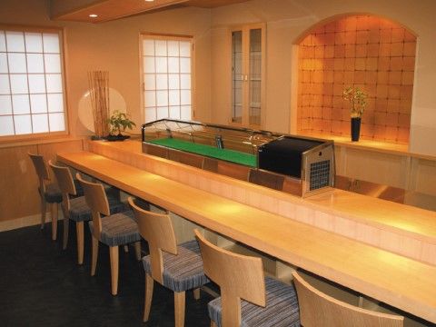 カウンターテーブルに椅子が配置されている。目の前には寿司ネタを入れる冷蔵機器がある。奥には植物も飾られている。
