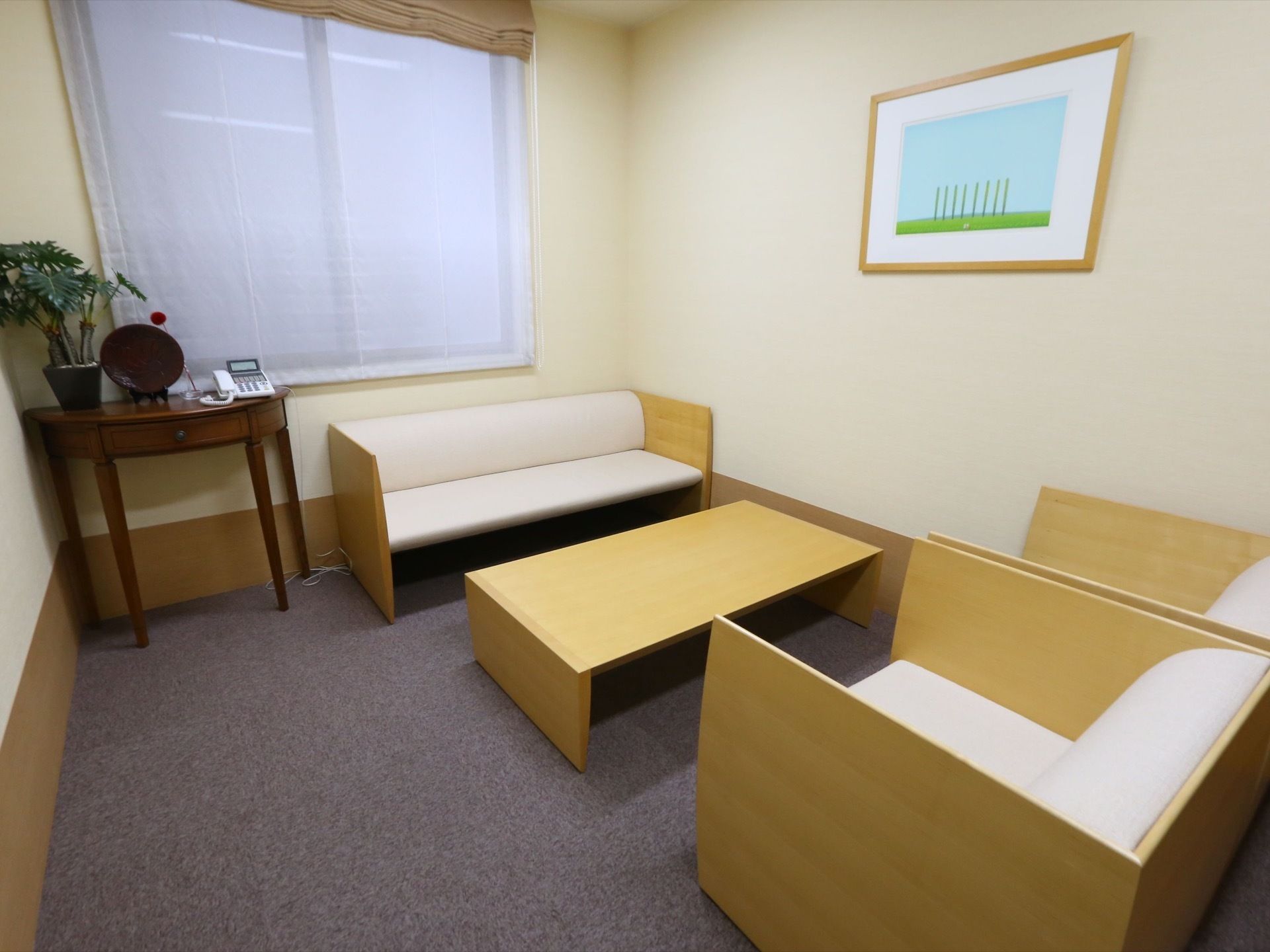 テーブルやソファーが設置された個室。窓際にある机の上には電話が置かれており、壁には絵が飾られている。