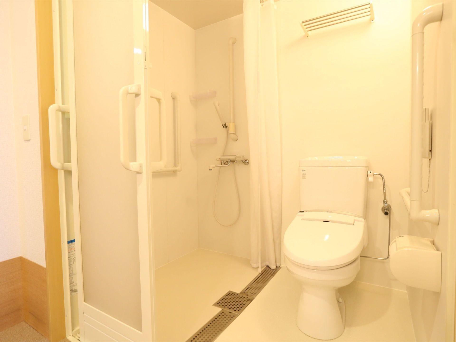 白を基調とした清潔感のあるトイレで、壁には手すりが設置されている。カーテンに仕切られてシャワー室が設置されている。