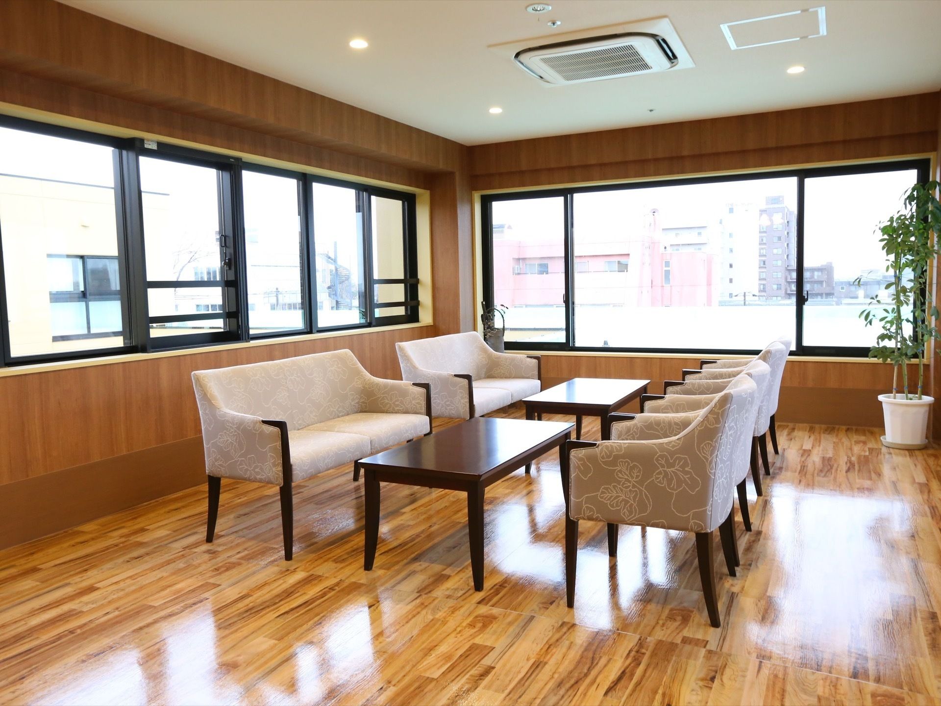フローリングの部屋に、ソファとローテーブルが置かれている。壁には窓があり、部屋の隅には観葉植物が置かれている。