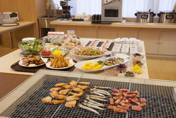 大皿に盛り付けられた海老フライや野菜の煮物やサラダが並ぶテーブルと魚や肉を焼いているバーベキューコンロ