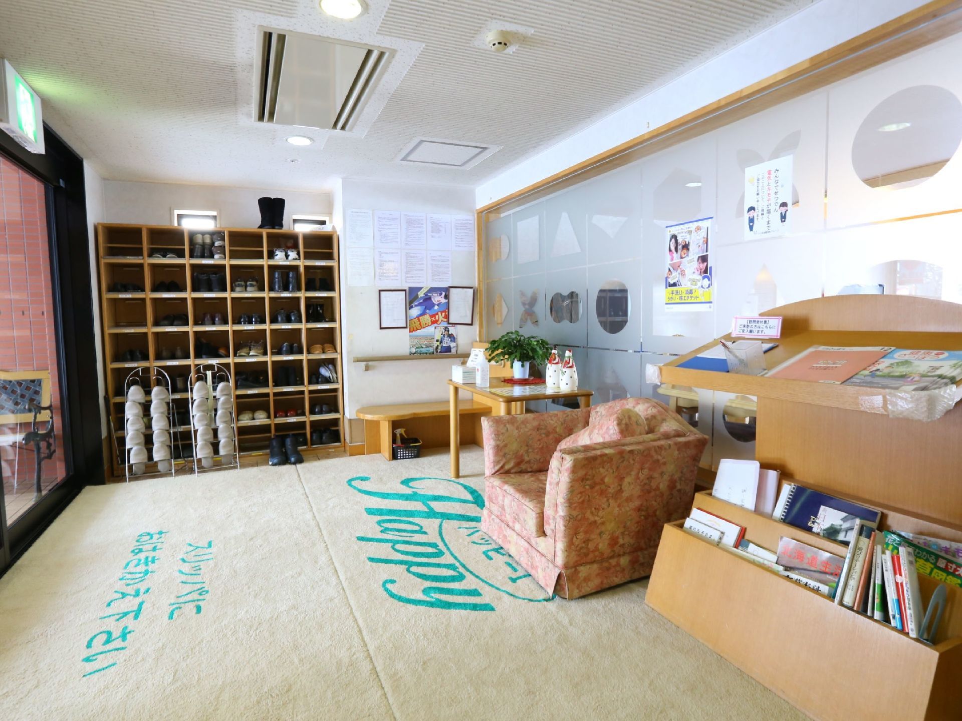 エントランスはロゴ入りの大きな絨毯が敷かれている。奥の壁に下駄箱が取りつけられ、その前にスリッパが用意されている。