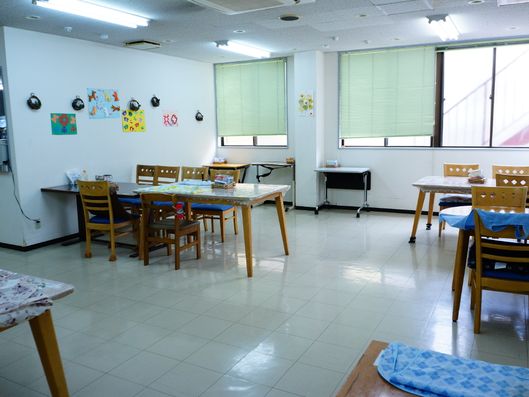 3脚ほどの椅子が置かれている。奥には窓があり、ブラインドが付いている。"