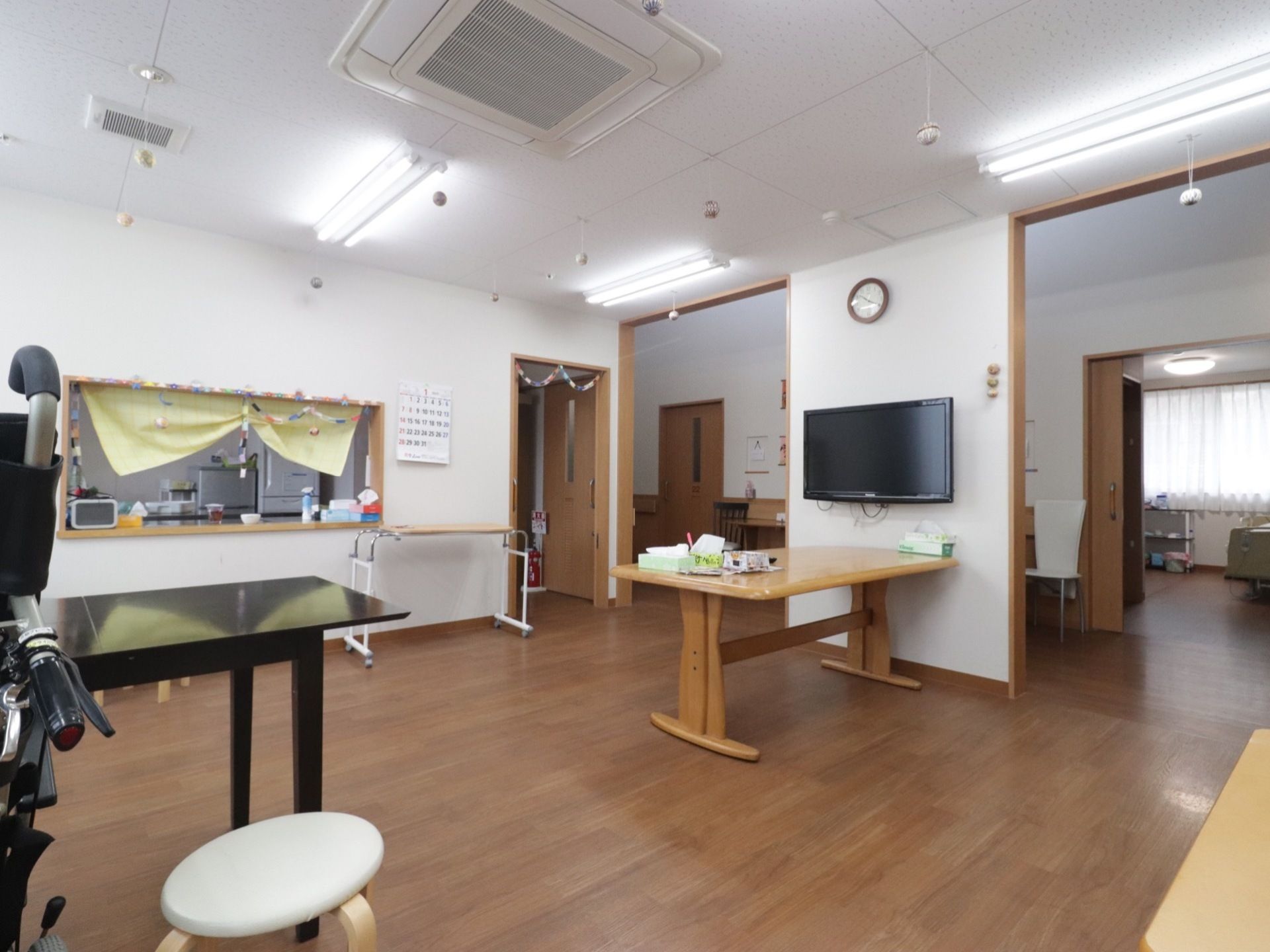 食堂内には照明が多く明るい。エアコンが天井に設置され、壁にはテレビが置かれている。厨房内には消火器がある。