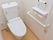 居室内のトイレはナチュラルな色の木目の床になっている。便器や手すりなどの設備ははすべて白で統一されている。