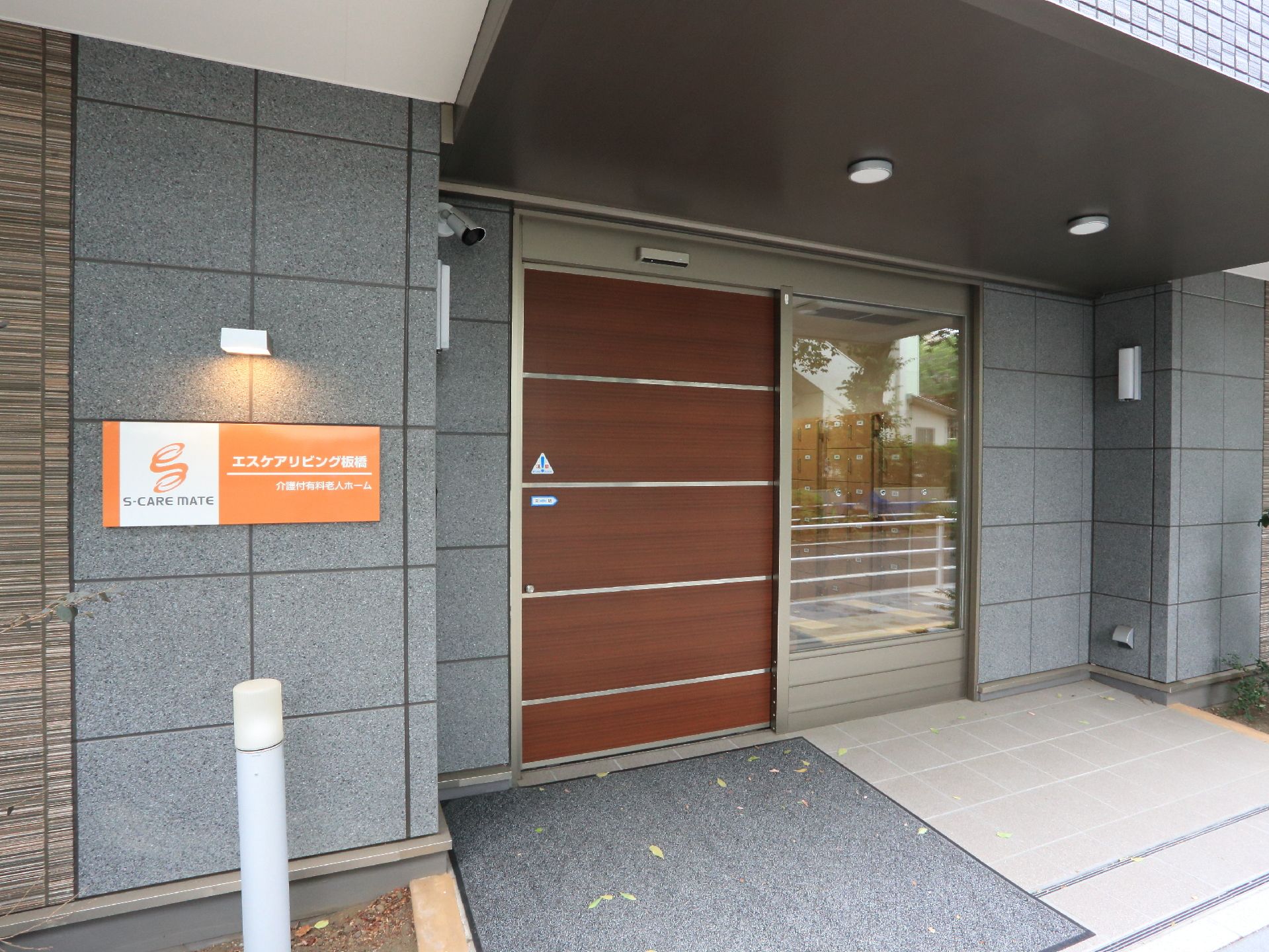 玄関は自動ドア。木目調のドアがシックな印象。フラットな床には滑り止めの大きなマットが敷いてあり足元も安心。