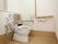段差のない床の上に洋式トイレが設置してある。ウォシュレットタイプで、壁には緊急時呼び出しのブザーがある。手すりが設置してある。