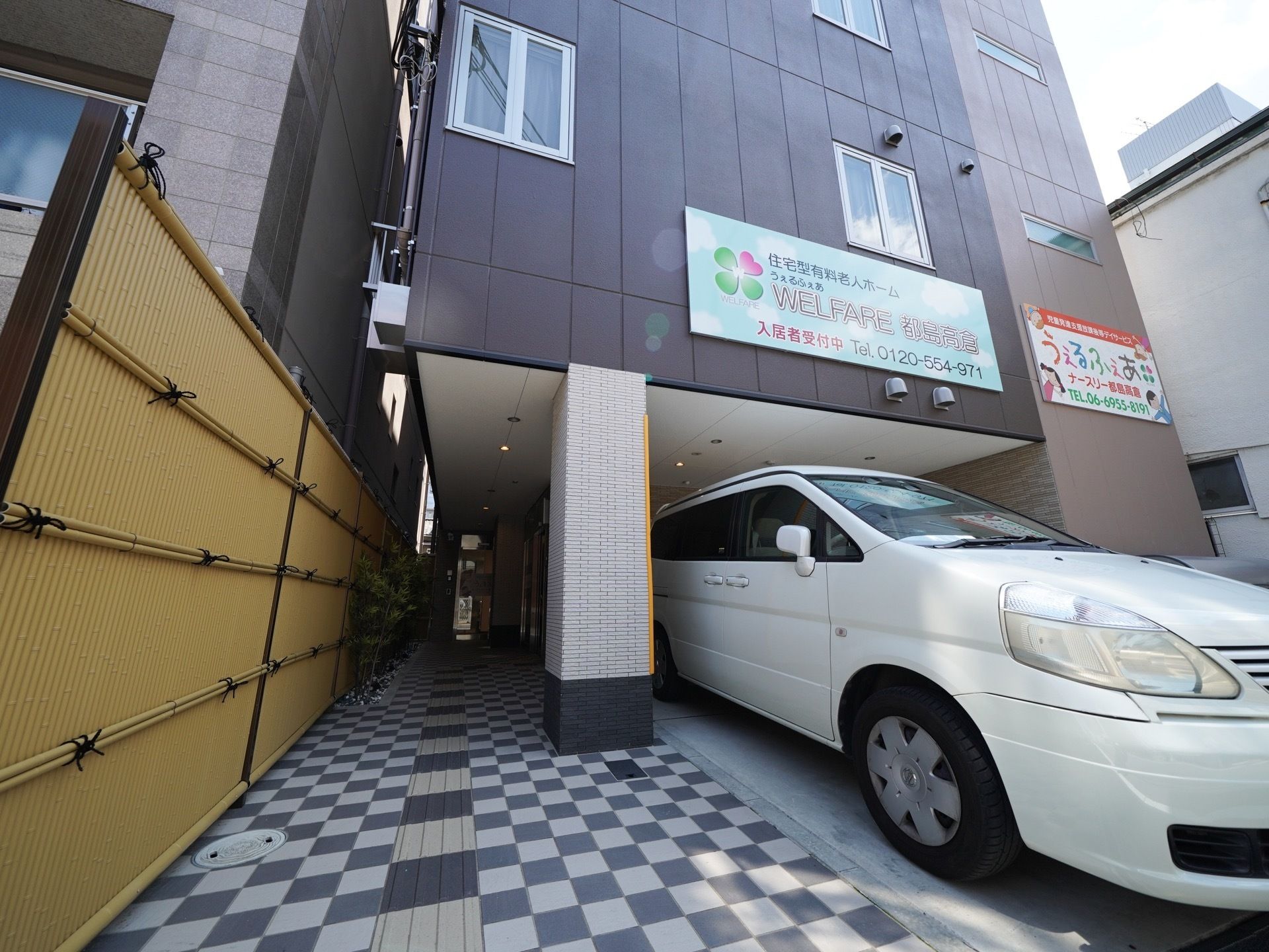 通常のマンションのような落ち着いた雰囲気の外観で、施設名の看板が掲げられている。隣のマンションとの境に竹のフェンスが設置されている。