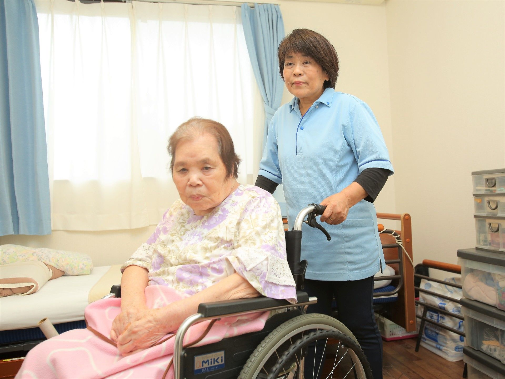 居室にて、利用者が座っている車椅子を女性スタッフが押している様子