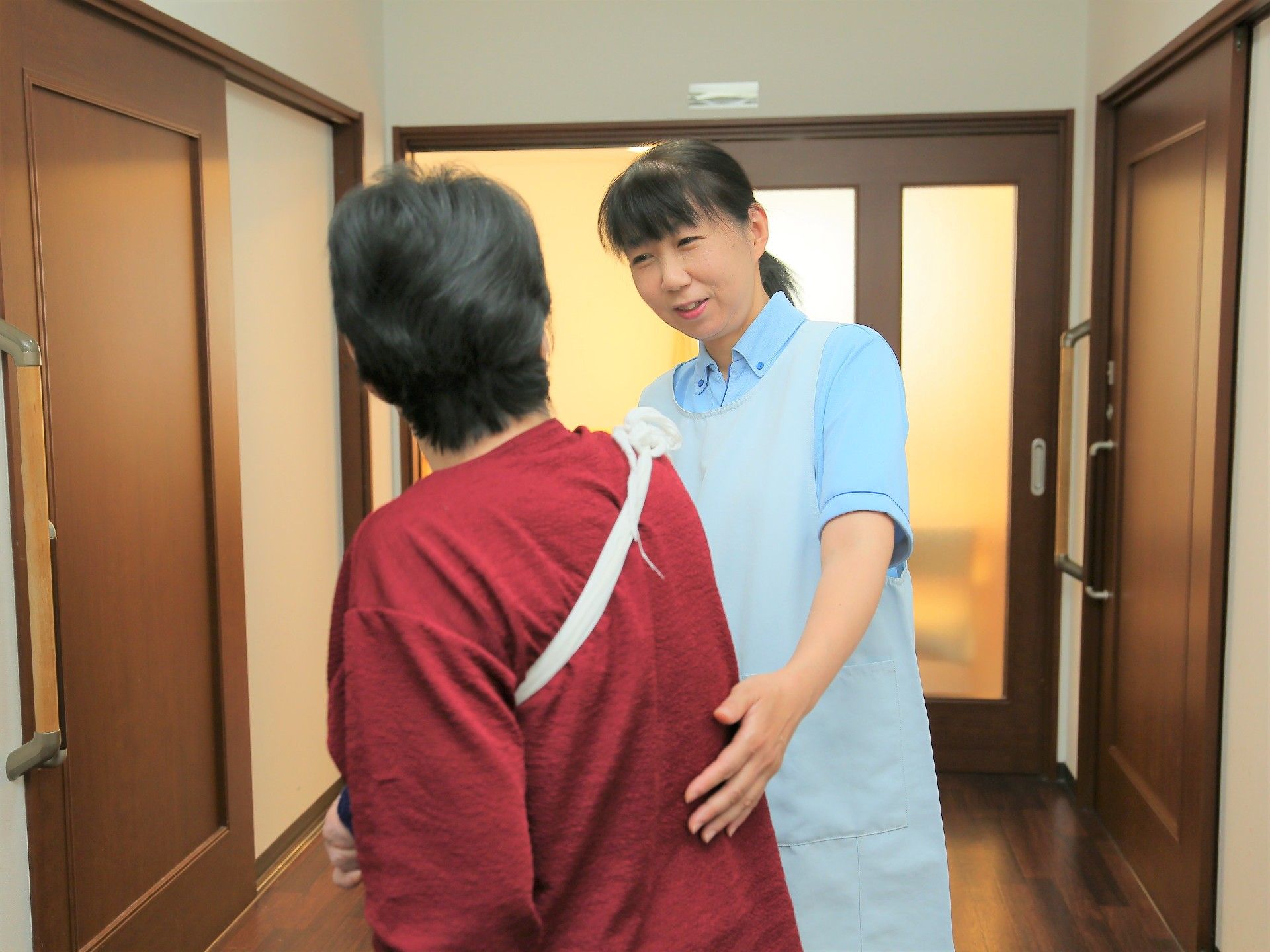 女性スタッフがご利用者様の腰に手を添えながら、歩行を支えている様子