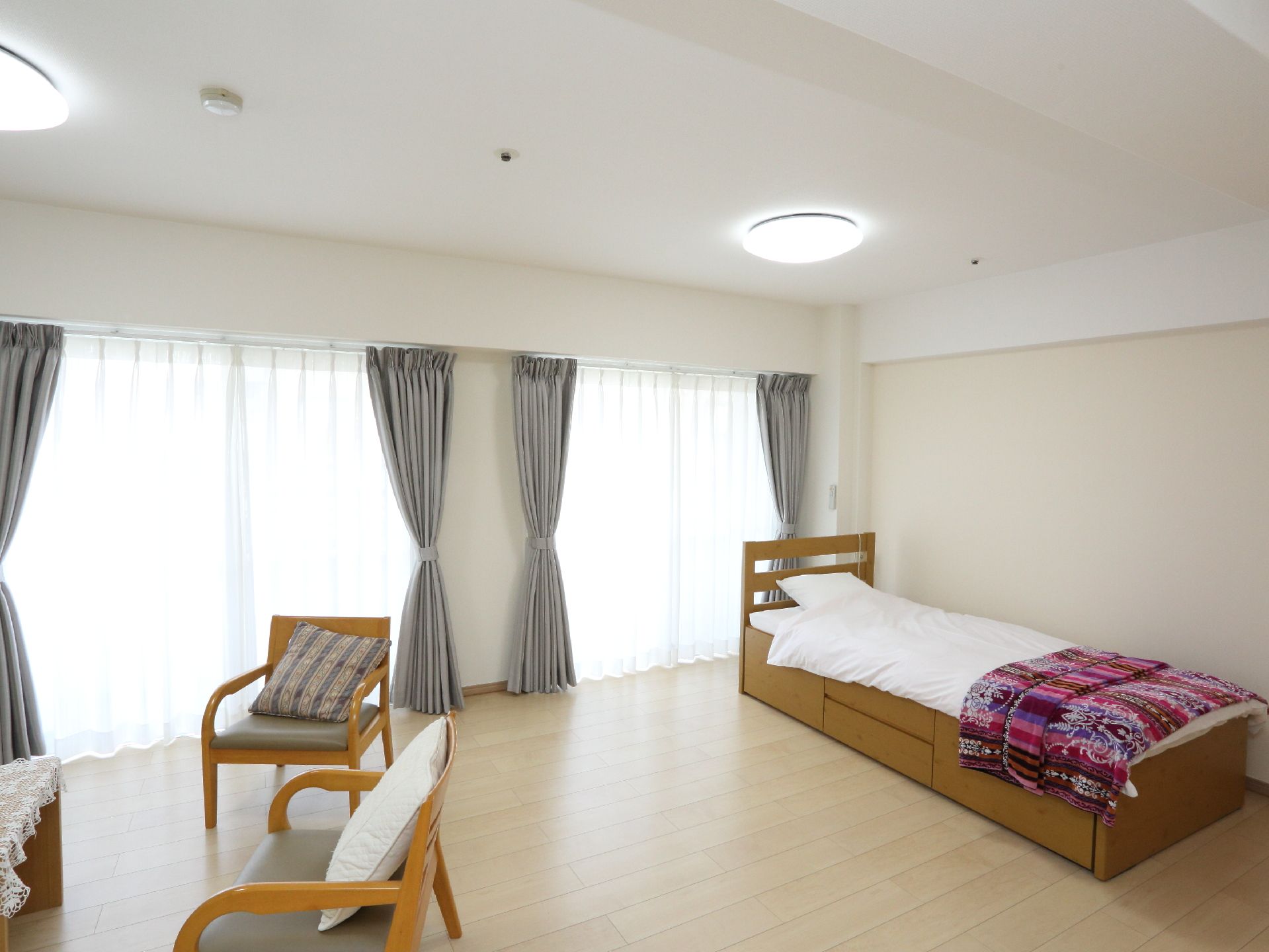 居室の壁は白色で床はフローリングになっている。大きな窓が2ヶ所にあり、開放的な部屋である。ベッドやテーブル、椅子などが置かれている。
