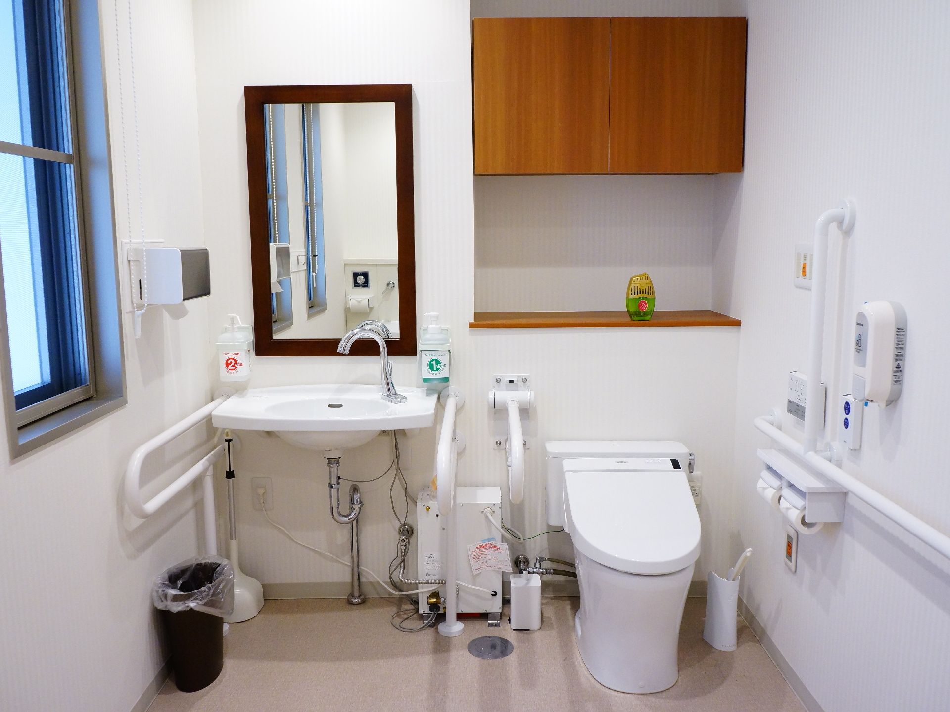 フラットなスペースにトイレと洗面台が並んでいる。壁には座り立ち動作をサポートする手すりが複数設置されている。