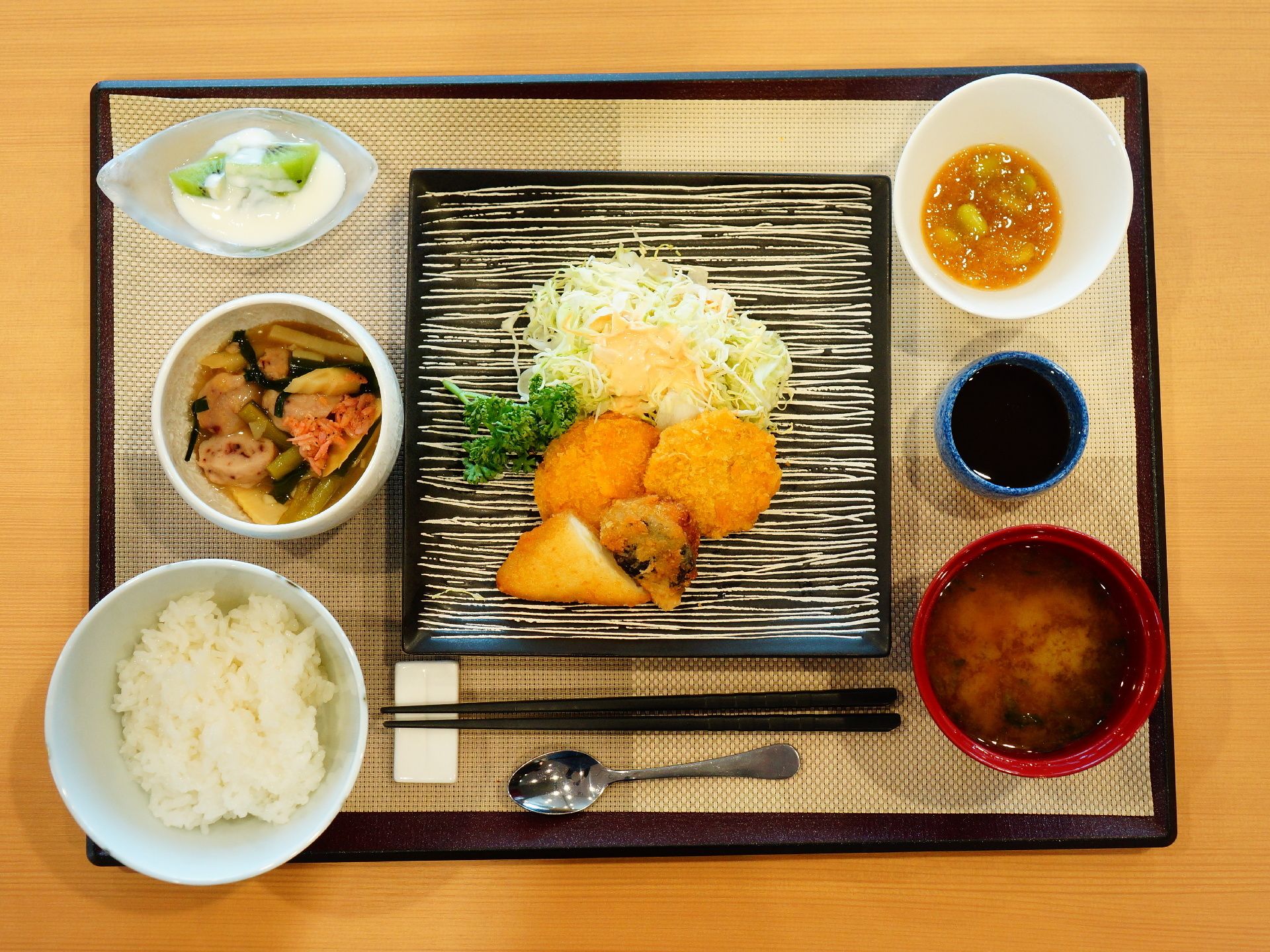 ブラウンのトレーの上に1人分の食事がセットされている。手前には箸置きと箸、スプーンが置かれ、複数の食器が並んでいる。