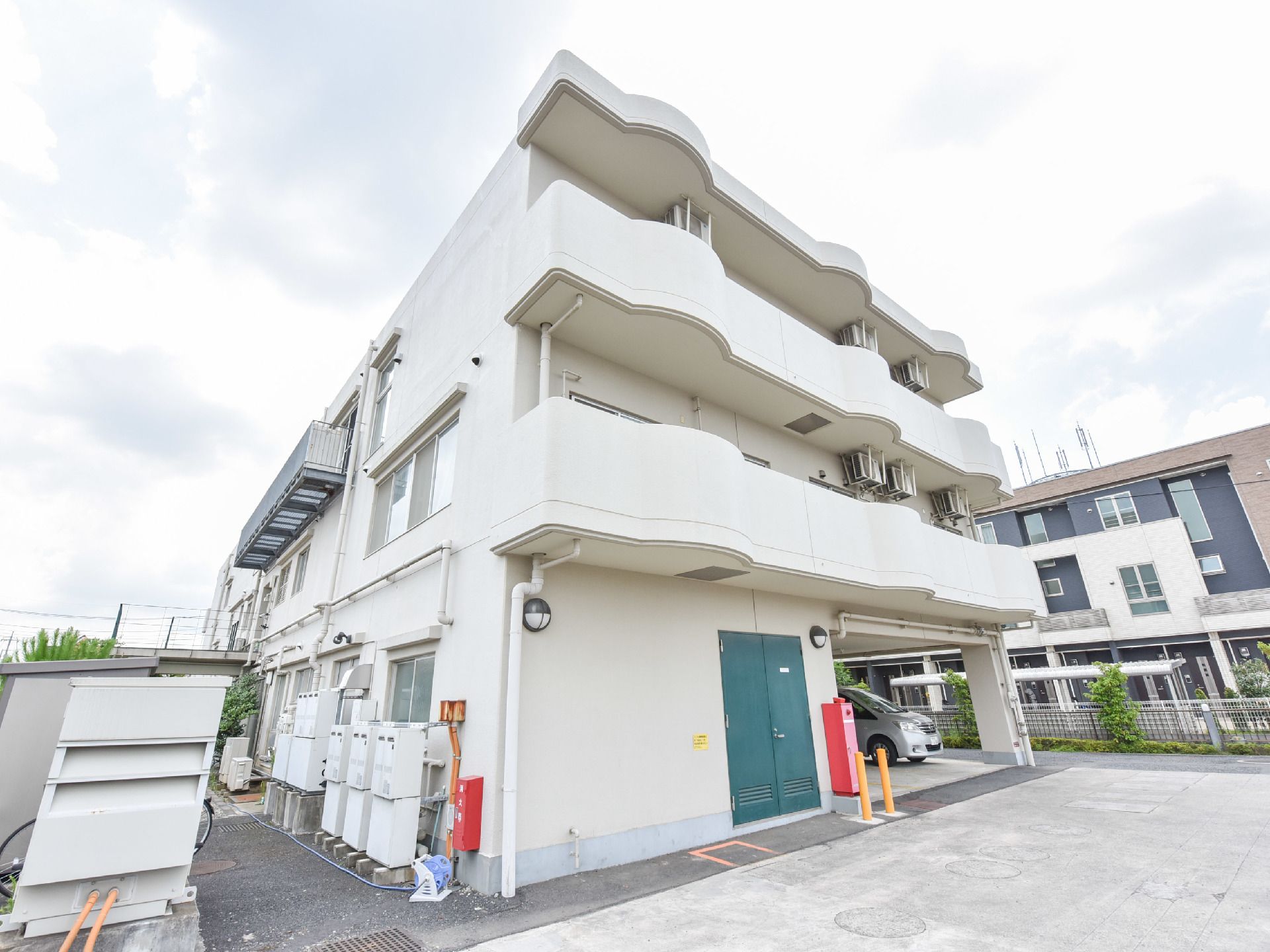 RC造の3階建てで白色の外壁の施設である。手前側の2階からバルコニーになっている。1階には消火設備が設置してある。